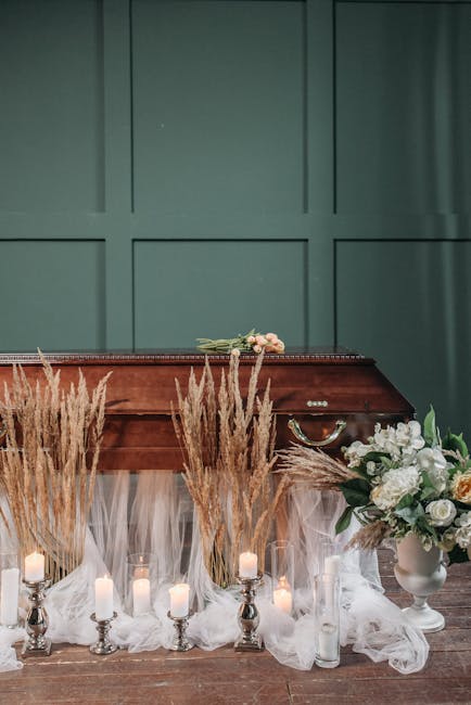 A floral arrangement for a funeral display featuring predominantly white roses and lilies with touches of soft pink blooms, arranged in a white vase. The flowers are fresh with tender petals and sturd