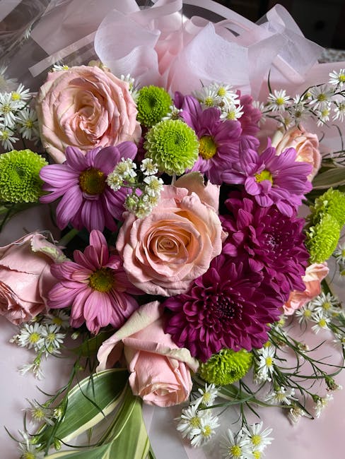 A vibrant floral arrangement featuring soft pink roses with delicate, layered petals, complemented by bright purple daisies with yellow centers, and fresh green chrysanthemums with round, compact bloo